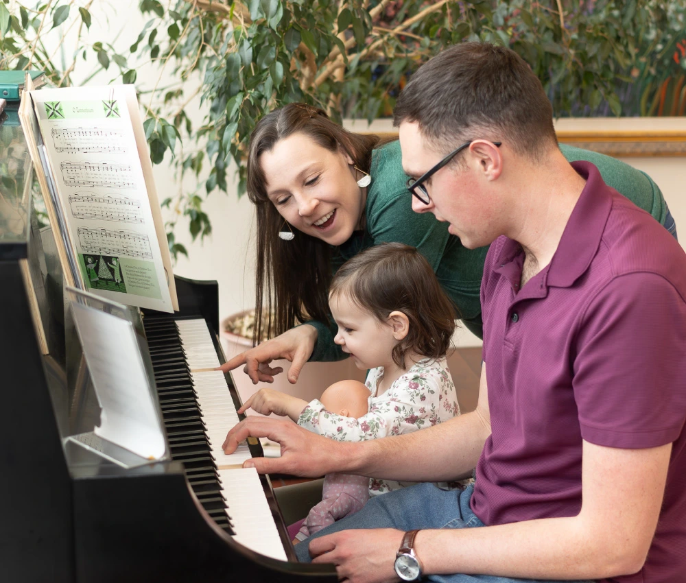 mother, father and daughter sitting and playing together at a piano