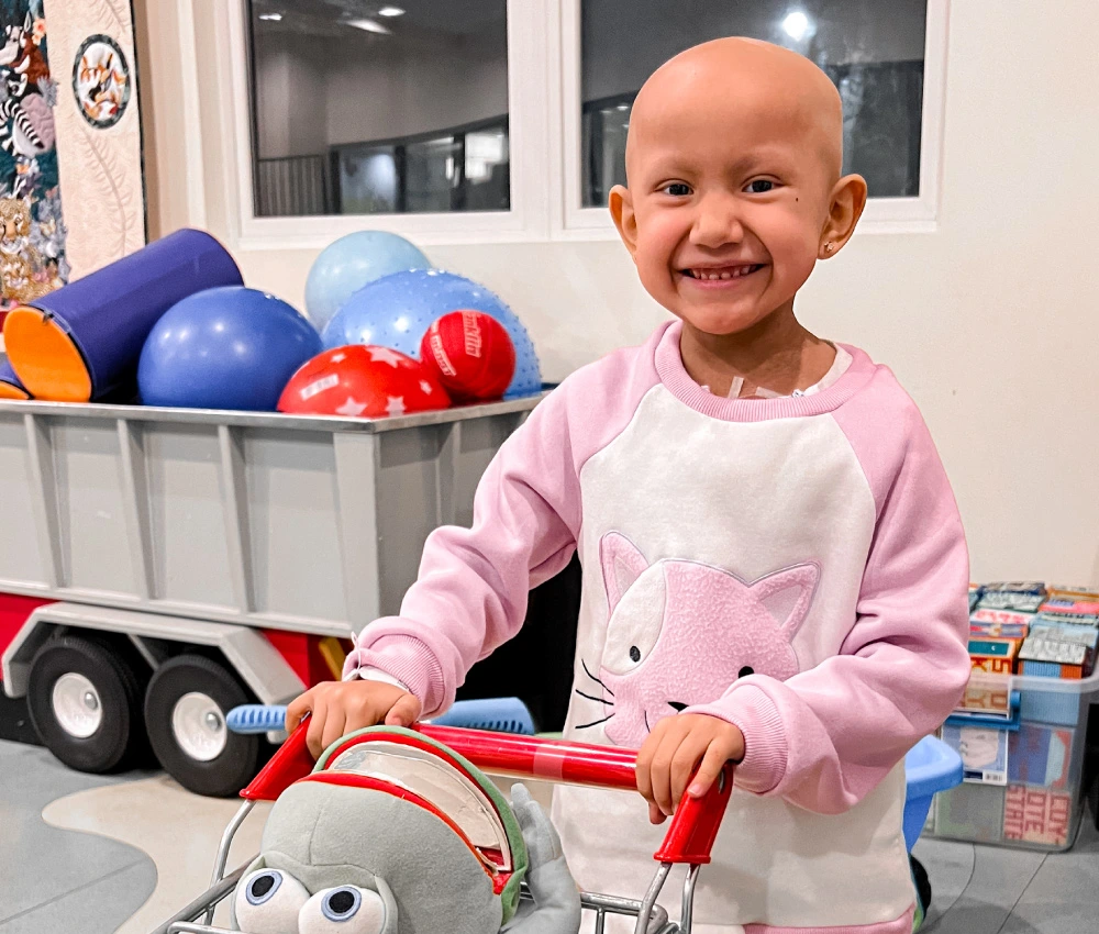 Jayline smiling wearing a pink sweater and playing with a toy shopping cart